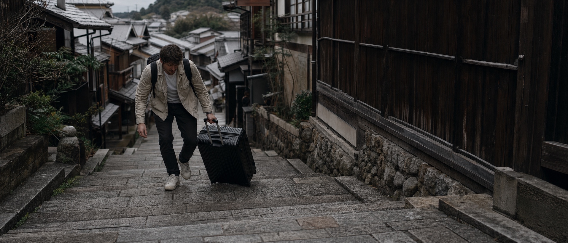 京都の石段で大きなスーツケースを運ぶのに苦労する外国人旅行者